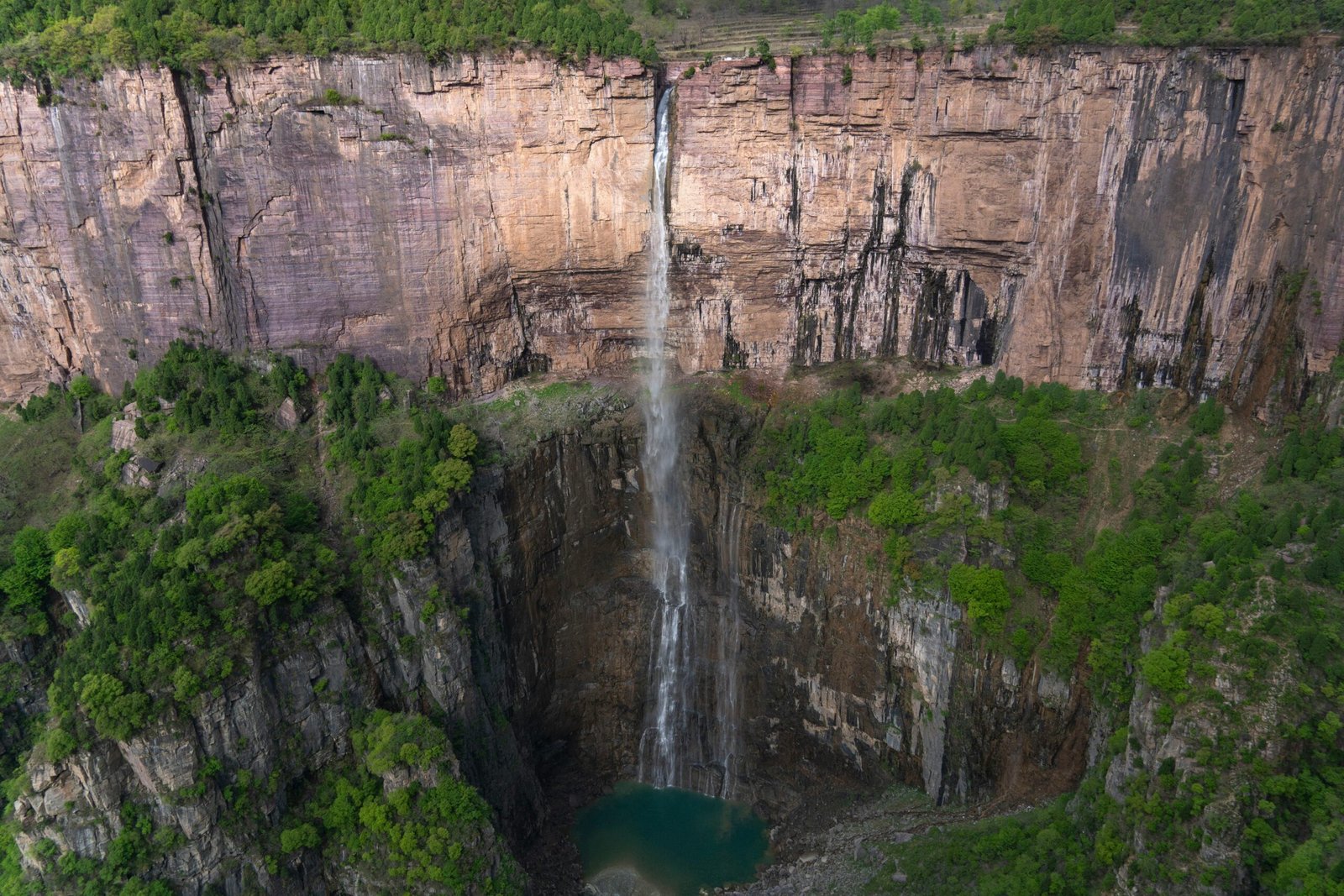 A stunning aerial view of a waterfall cascading down rocky cliffs surrounded by lush greenery in Xinxiang, China.
