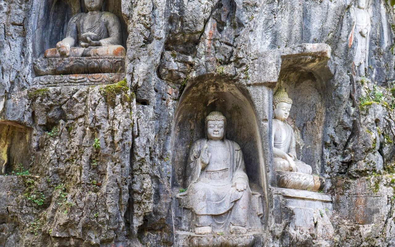 Explore serene Buddha sculptures intricately carved into a rugged rocky cliff face.