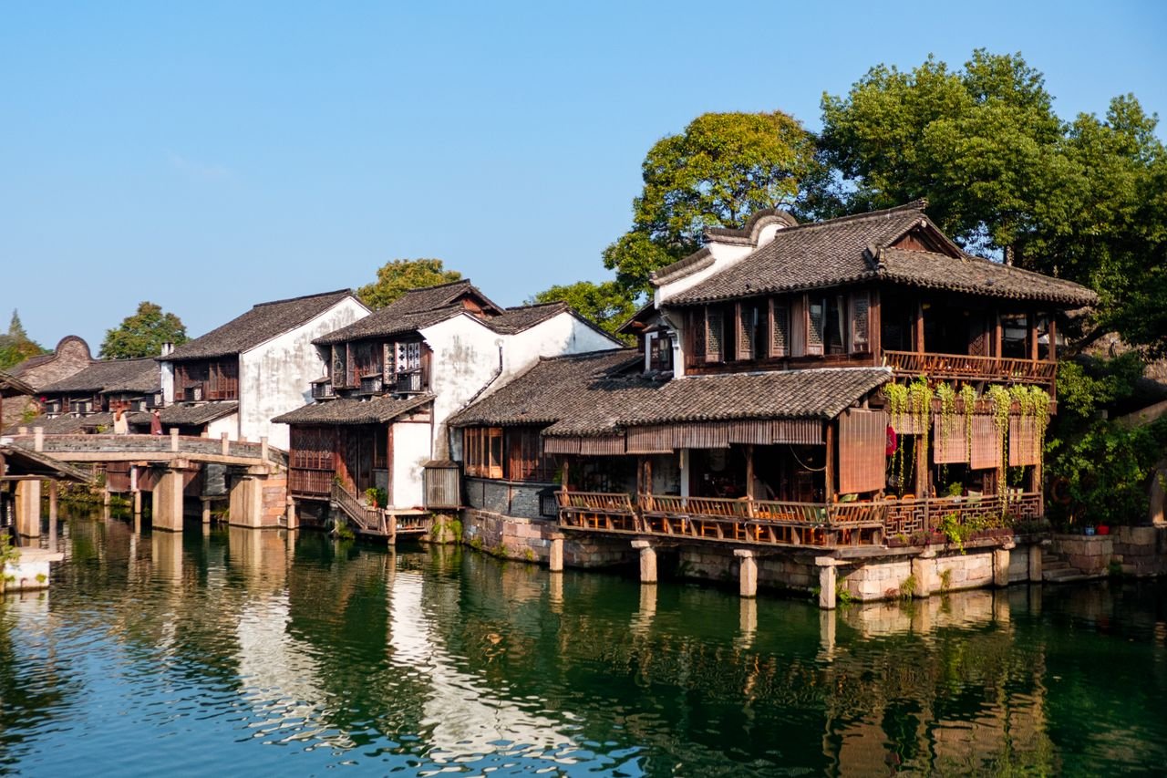 Scenic view of a traditional Chinese water town with wooden architecture reflected in a calm river.